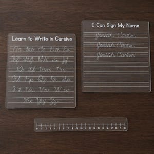 May include: Two clear acrylic practice boards and a ruler. One board is labeled "Learn to Write in Cursive" with the alphabet. The other is labeled "I Can Sign My Name" with lines. The clear ruler shows measurements from 0 to 20 inches.