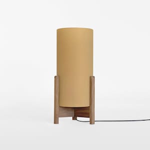 May include: A modern floor lamp with a light brown wooden base and a cylindrical, light yellow lampshade.