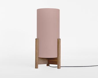 May include: A pink cylindrical lampshade sits on a wooden tripod stand. The lamp has a black cord.