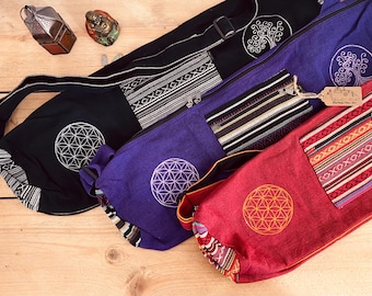 May include: Three yoga mat bags with different designs. The first bag is black with a white flower of life design. The second bag is purple with a white flower of life design. The third bag is red with an orange flower of life design.