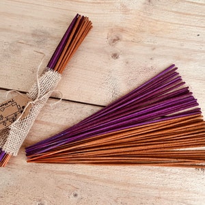 May include: Two bundles of incense sticks, one wrapped in burlap with a brown paper tag that says "The Little Happy Box", and the other bundle is unwrapped. The sticks are brown and purple.