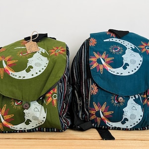 Può includere: Due zaini con stampa di luna crescente e sole. Uno zaino è verde oliva, l'altro è verde acqua. Entrambi presentano pannelli laterali neri con strisce verticali multicolori, una patta superiore con chiusura a bottone e un cartellino di carta.