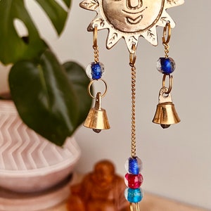 Brass wind chime with a crescent moon, star, and sun design. The chime has blue and red beads and bells. Handmade Fair Trade Ethically Sourced Bohemian Hippie Bell