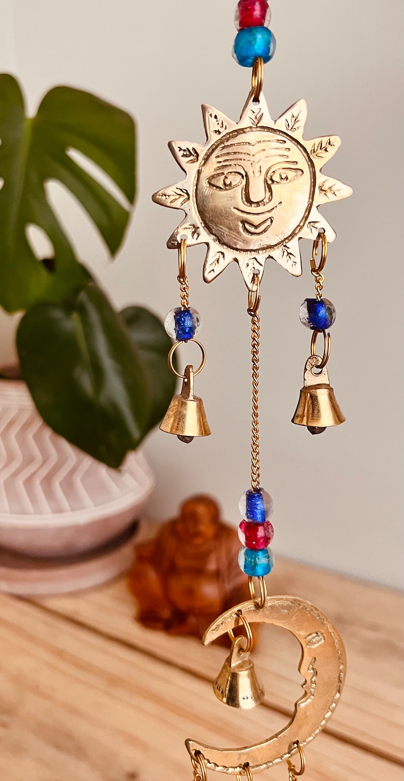 Brass wind chime with a crescent moon, star, and sun design. The chime has blue and red beads and bells. Handmade Fair Trade Ethically Sourced Bohemian Hippie Bell