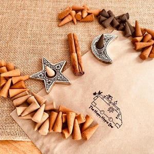 May include: A selection of brown incense cones, displayed with star and crescent moon incense holders. Two cinnamon sticks are also visible. The image includes the text "The Happy Hippie Bus".