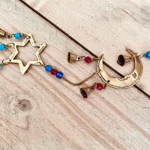 Brass wind chime with a crescent moon, star, and sun design. The chime has blue and red beads and bells. Handmade Fair Trade Ethically Sourced Bohemian Hippie Bell
