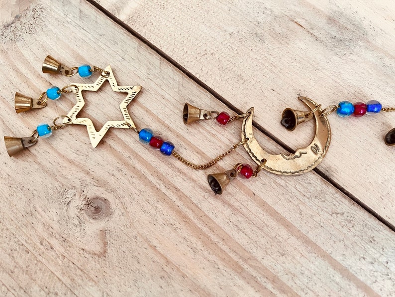 Brass wind chime with a crescent moon, star, and sun design. The chime has blue and red beads and bells. Handmade Fair Trade Ethically Sourced Bohemian Hippie Bell
