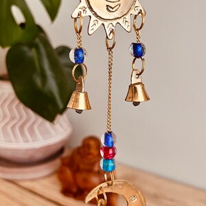 Brass wind chime with a crescent moon, star, and sun design. The chime has blue and red beads and bells. Handmade Fair Trade Ethically Sourced Bohemian Hippie Bell