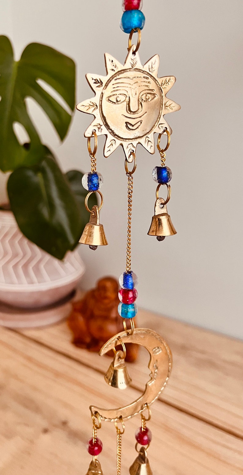 Brass wind chime with a crescent moon, star, and sun design. The chime has blue and red beads and bells. Handmade Fair Trade Ethically Sourced Bohemian Hippie Bell