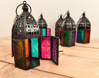 May include: Set of five black metal lanterns with colorful stained glass panels. The lanterns have intricate cutouts and are perfect for adding a touch of Moroccan style to your home decor.