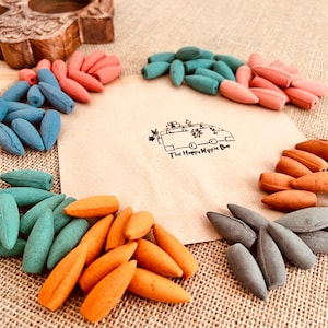 Op de afbeelding: Een assortiment kleurrijke wierookkegels in tinten blauw, teal, koraal, oranje en grijs zijn gerangschikt rond een papier met een logo. Een houten gesneden kandelaar staat op de achtergrond. Het logo The Happy Hippie Bus is zichtbaar.