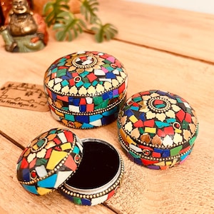 Puede incluir: Tres joyeros de mosaico con patrones de azulejos coloridos e irregulares. Las cajas son redondas con adornos dorados y un interior de terciopelo negro. Una caja está abierta.