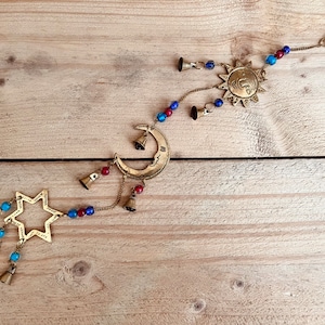 Brass wind chime with a crescent moon, star, and sun design. The chime has blue and red beads and bells. Handmade Fair Trade Ethically Sourced Bohemian Hippie Bell