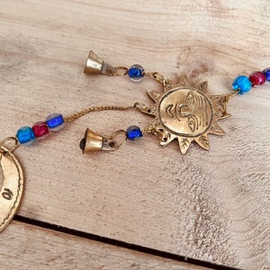 Brass wind chime with a crescent moon, star, and sun design. The chime has blue and red beads and bells. Handmade Fair Trade Ethically Sourced Bohemian Hippie Bell