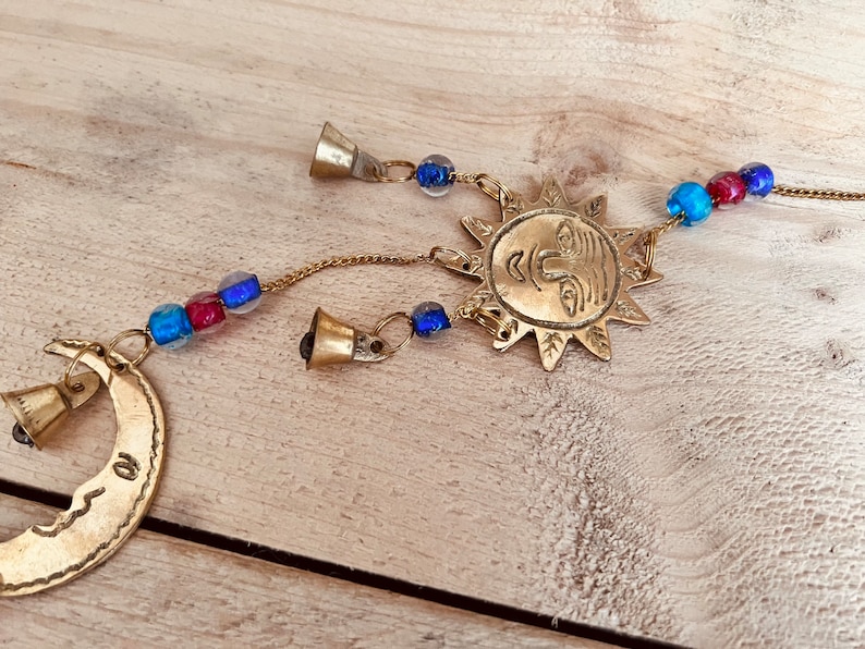 Brass wind chime with a crescent moon, star, and sun design. The chime has blue and red beads and bells. Handmade Fair Trade Ethically Sourced Bohemian Hippie Bell