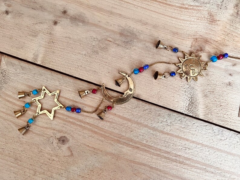 Brass wind chime with a crescent moon, star, and sun design. The chime has blue and red beads and bells. Handmade Fair Trade Ethically Sourced Bohemian Hippie Bell