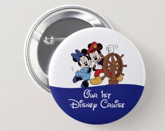 May include: A round button with a white background and a blue lower section. The button features Mickey and Minnie Mouse, with Mickey at the ship's wheel. Text reads "Our 1st Disney Cruise". The button is silver.