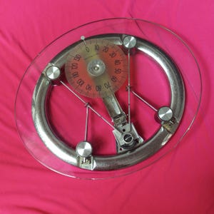 May include: A vintage bathroom scale with a clear glass top and a silver-coloured metal frame. The scale features a circular dial with numbers and a red centre. The scale measures up to 59 kg.