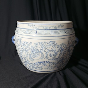 Peut inclure: Pot de fleurs en céramique blanche avec des motifs floraux et géométriques bleus. Le pot a deux poignées bleues et une large ouverture. Le motif comprend une grande fleur et des volutes. Pour l'intérieur ou l'extérieur.