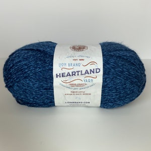 Puede incluir: Una madeja de hilo Lion Brand Heartland en una combinación de colores azul y gris. La etiqueta dice "Lion Brand Heartland Yarn - Hand-Crafts - Artisanat - Sensationally Soft - Sensation Douce - Premium Acrylic - Acyclique de Qualite Superieure - LionBrand.com".