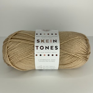 May include: A skein of beige acrylic yarn called "Tones" by Lion Brand. The label says "Basic Stitch Anti-Pilling Acrylic Yarn" and "For Your Perfect Match". It also says "3.5 oz / 100 g" and "185 yd / 170 m".