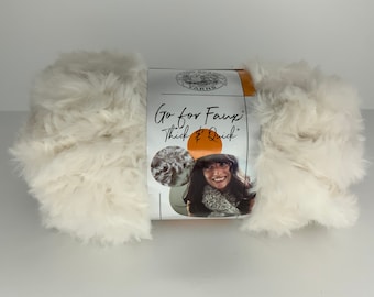 May include: A skein of white faux fur yarn with a label that reads "Go for Faux! Thick & Quick" and features a woman wearing a scarf made from the yarn.