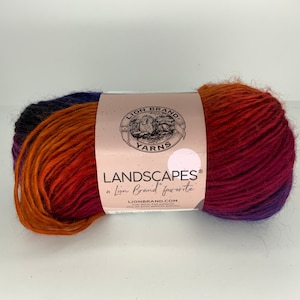 May include: A skein of Lion Brand Landscapes yarn in a gradient of orange, red, and purple. The label reads "Landscapes, a Lion Brand favorite".