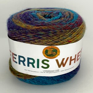 May include: A skein of Lion Brand Ferris Wheel yarn in a multi-colored pattern of teal, purple, brown, and yellow. The yarn is wrapped around a white label with the Lion Brand logo and the text "Ferris Wheel" and "Over 7500 free patterns! Plus de 7500 gabarits gratuits! / Sobre 7500 patrones gratis! LIONBRAND.COM".