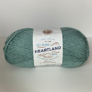 May include: A skein of Lion Brand Heartland Yarn in a muted teal color. The label reads "Heartland Yarn" with the words "Hand-Crafts - Artisanat - Sensationally Soft - Sensation Douce". The yarn is premium acrylic.