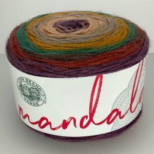 May include: A ball of Lion Brand Mandala yarn in the "Autumn Leaves" colourway. The yarn is a multi-coloured gradient of purple, brown, green, yellow, and beige.