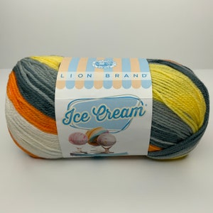 May include: A skein of Lion Brand Ice Cream yarn in a multi-colored stripe pattern. The yarn is yellow, orange, white, and gray.