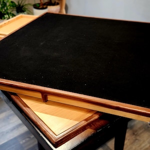 May include: A wooden game table with a black playing surface and four pull-out drawers. The table has a dark brown border and light brown drawers. The table is approximately 91 cm square.