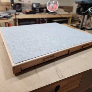 May include: A rectangular wooden tray with a light gray felt surface. The tray has a natural wood frame with visible joinery details. The felt is flush with the frame. The tray is sitting on a wooden surface.