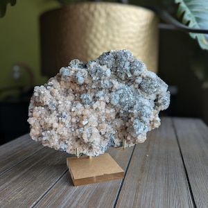 以下が含まれることがあります： 自然の鉱物標本。 ピーチ、グレー、透明な結晶が混ざり合っています。 鉱物は小さな金色のスタンドに取り付けられています。 背景はぼやけています。 全体的な美しさは、自然の要素と地質学的な美しさに焦点を当てていることを示唆しています。