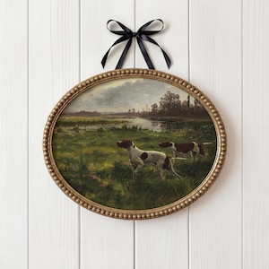 May include: Oval framed artwork featuring a landscape with two dogs in a field. The dogs are white with brown spots. The frame is gold with a beaded edge, and a black ribbon is tied at the top for hanging.