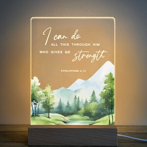 May include: A light-up sign with a watercolour landscape scene of mountains, trees, and a river. The sign has the text "I can do all this through him who gives me strength Philippians 4:13".