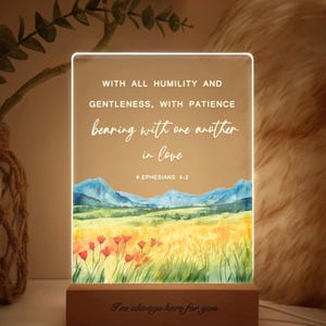 May include: A rectangular LED night light with a wooden base. The light features a watercolor landscape with mountains, fields, and flowers. Text includes a Bible verse and the phrase "I'm always here for you."