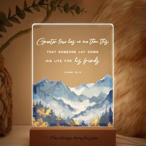 May include: An illuminated rectangular sign with a wooden base. The sign features a mountain scene and the text "Greater love has no one than this..." and "I'm always here for you."