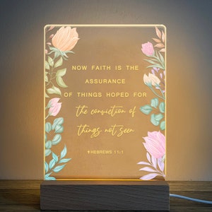 May include: A light-up sign with a floral design and the quote "Now faith is the assurance of things hoped for, the conviction of things not seen."  The quote is attributed to Hebrews 11:1.