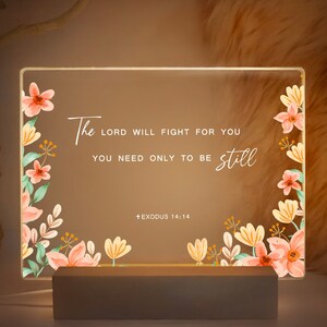 May include: A light-up sign with a floral design and the quote "The Lord will fight for you, you need only to be still."  The quote is attributed to Exodus 14:14.