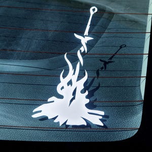 May include: A white vinyl decal of a sword in a bonfire, a popular symbol from the video game Dark Souls.