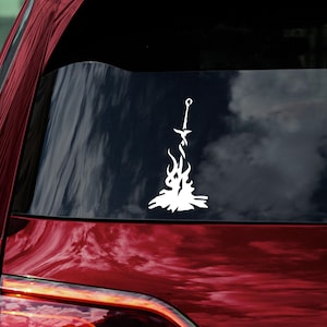 May include: White vinyl decal of a sword in a bonfire, a popular symbol from the video game Dark Souls.