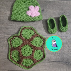 May include: A green crocheted turtle hat with a pink flower, a green crocheted turtle shell, and two green crocheted booties. The set is made by Dreams of Thread.