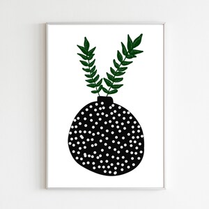 Pode incluir: Uma impressão de arte emoldurada com um vaso preto com bolinhas brancas, segurando dois ramos de folhas verdes. A obra de arte é definida contra um fundo branco, criando uma estética minimalista e moderna. A impressão está emoldurada em uma moldura prateada.