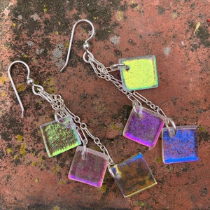 May include: A pair of silver chain earrings with iridescent square glass charms. The charms are in shades of green, purple, and blue.