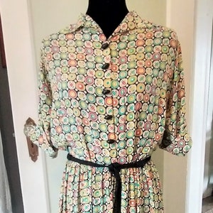 May include: A vintage dress with a black background and a colourful geometric pattern. The dress has a button-up front, a black belt, and a full skirt.