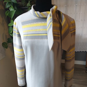 Puede incluir: Un vestido gris con rayas amarillas y plateadas. El vestido tiene manga larga y una corbata en el cuello.