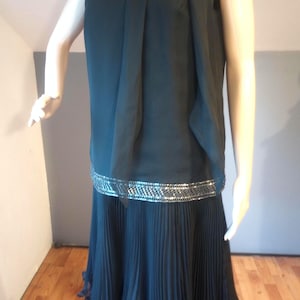 May include: A black sleeveless dress with a pleated skirt and a silver beaded trim. The dress has a high neckline and a bow at the neck.