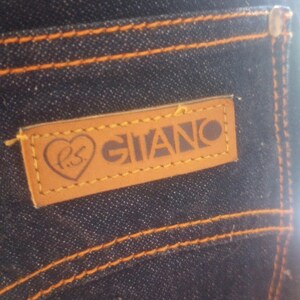 May include: Close-up of dark blue denim jeans with orange stitching. A brown leather patch on the back pocket features the word "GIANO" and a heart symbol with the letters "P.S."