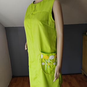 May include: A sleeveless, lime green dress with a front zipper and a pocket featuring a floral design. The pocket has white and yellow daisies with green stems and leaves. The dress is knee-length and appears to be made of a lightweight fabric.